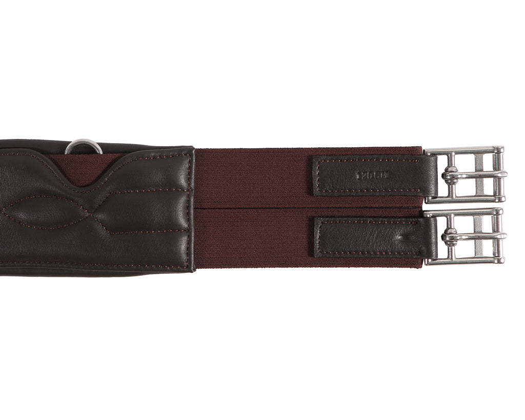 A close-up image of the Stud Guard Girth Comfort. It is made of soft padded leather with strong elastic ends. The girth features NDM cow sorting padding, leather with matching stitching, and 38mm heavy-duty elastic. It is designed for durability with top-quality leather and stainless steel buckles. The girth provides optimal protection and comfort for horses during jumping sessions. It has a center D ring for attaching breastplates and ensures a secure fit with its strong elastic ends. 
